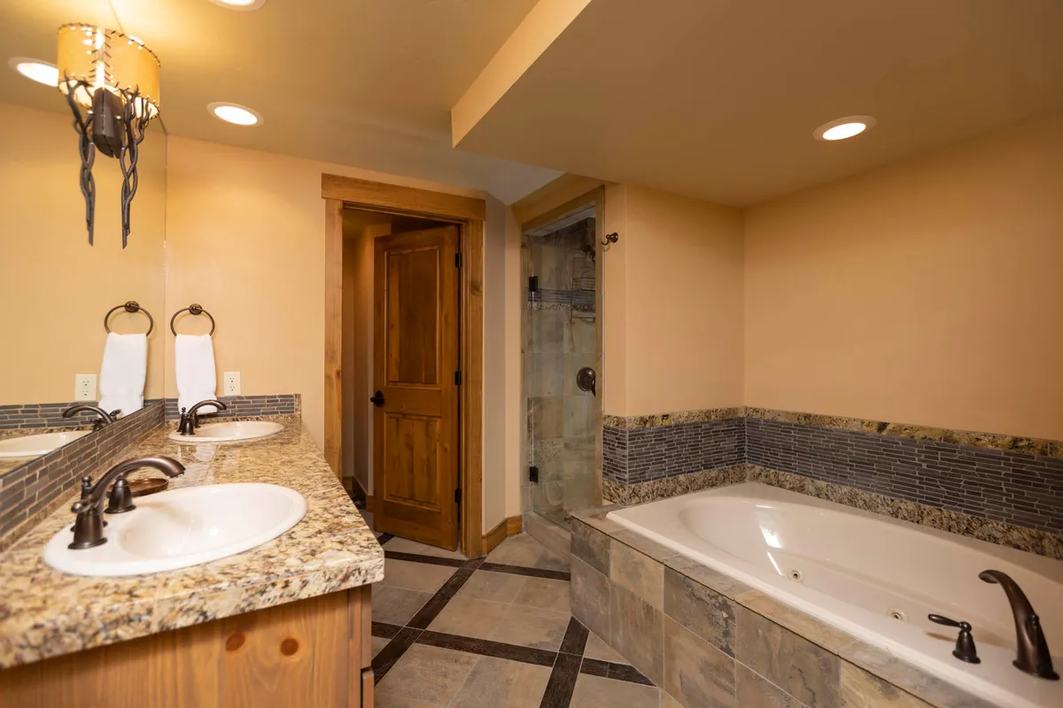 A modern bathroom with a large bathtub, double sinks on a granite countertop, and a textured wall. The space feels tranquil and luxurious, ideal for unwinding after a day on the slopes.