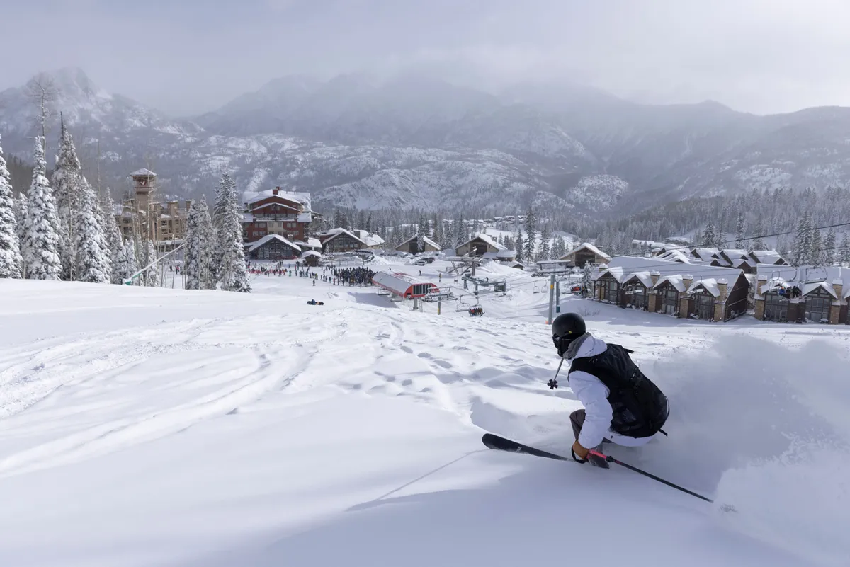 A skier carves through fresh snow, surrounded by snow-covered trees and with ski resort buildings visible in the background. This action-packed scene captures the excitement and family-friendly atmosphere of the slopes, highlighting the property's location right by the ski runs.