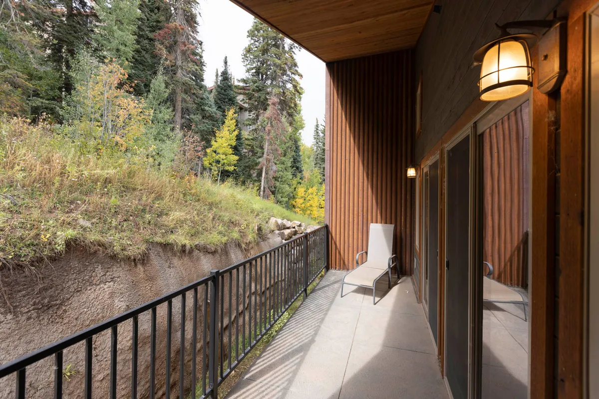A peaceful exterior deck with a wooden railing and a lone chair, framed by surrounding trees. The space invites moments of relaxation, watching wildlife, or enjoying a sunset view after a day of mountain adventures.