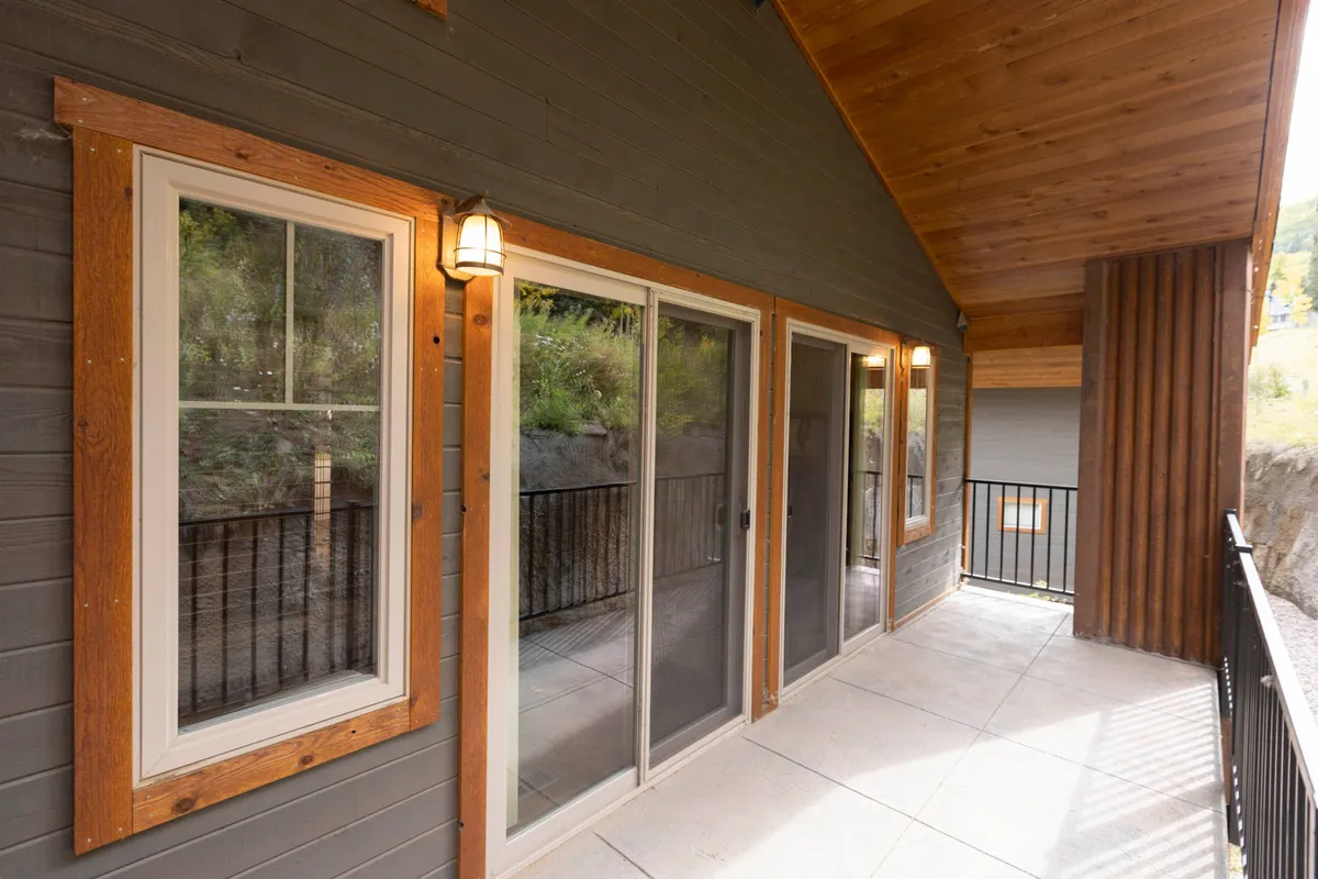 A view of the exterior of the property featuring large sliding glass doors, wooden accents, exposed beams, and an outdoor railing. The setup suggests easy access from the interior to the private deck, an inviting space for relaxation with plenty of natural light and a sense of connection to the outdoors.